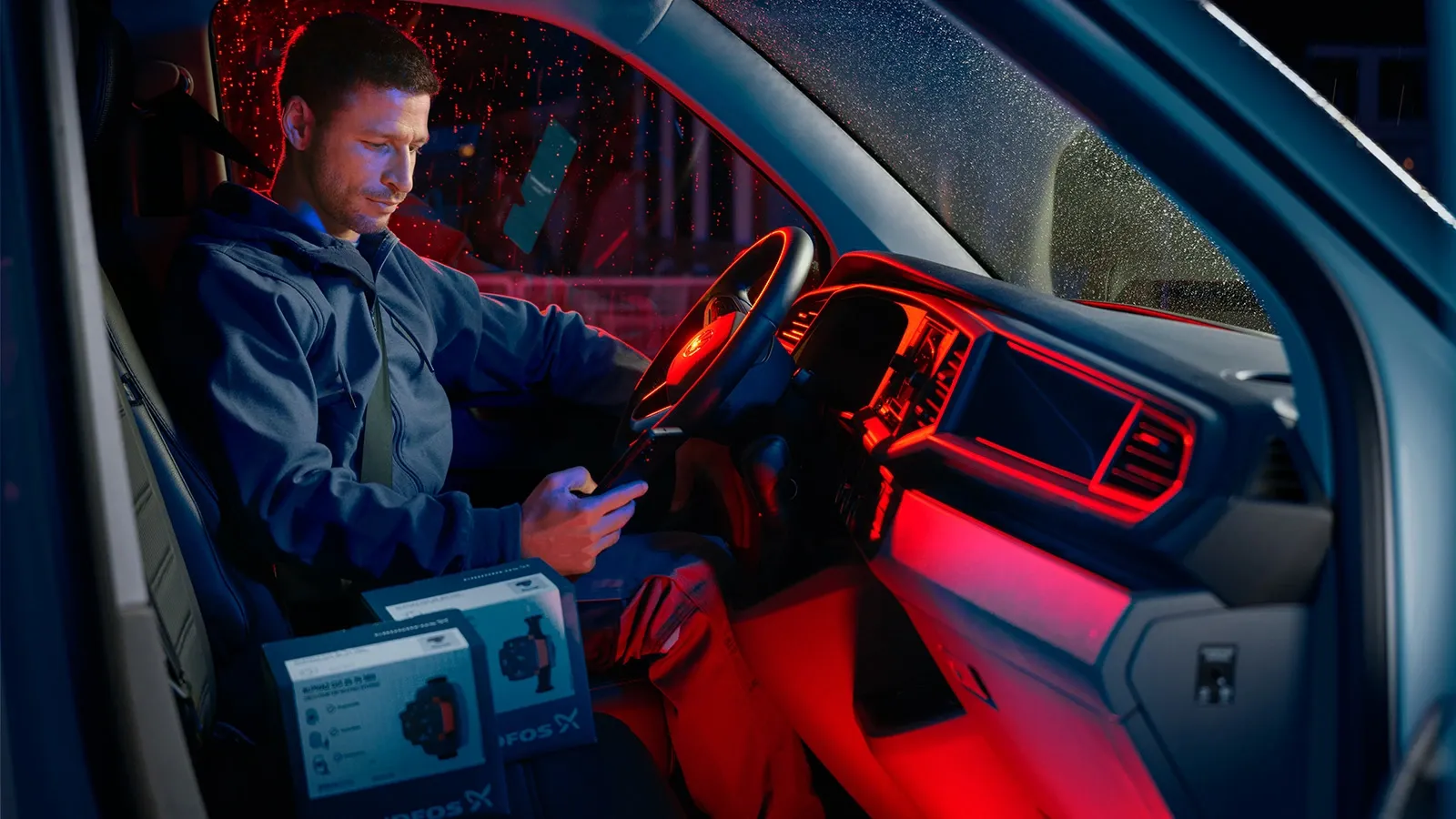Installateur im Lieferwagen mit Smartphone, daneben zwei Kartons mit Grundfos ALPHA GO Pumpen